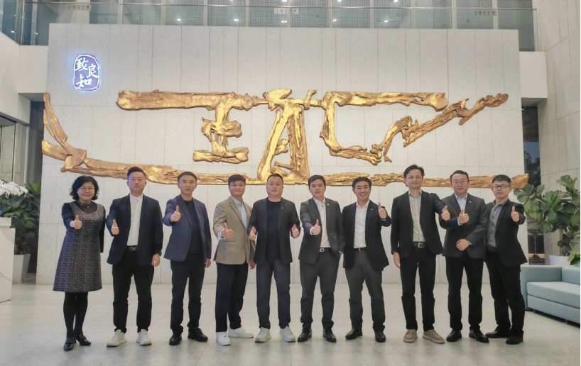 Group of business professionals posing together with thumbs up gesture in front of a corporate office wall with golden artwork